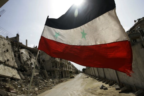 The Syrian flag flies among rubble