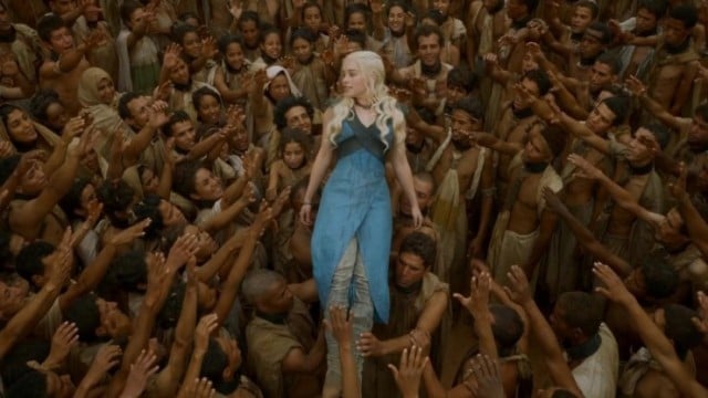 Daenerys Targaryen in a blue dress held up by the hands of a crowd of people in Season 3 finale of Game of Thrones
