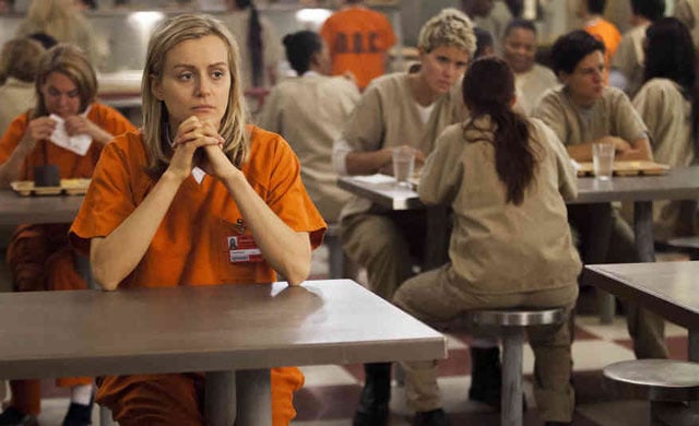 Taylor Schilling clasping her hands and sitting at a table in 'Orange is the New Black.'