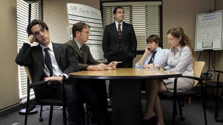 B.J. Novak, Rainn Wilson, Steve Carell, John Krasinski, and Jenn Fischer sitting around a table in a conference room on 'The Office'
