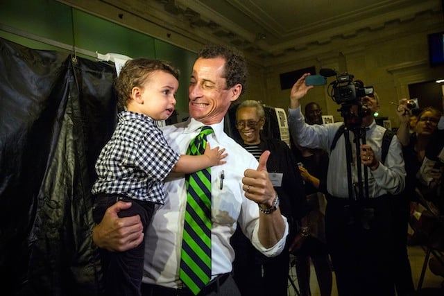 Anthony Weiner is giving a thumbs up while holding a child.