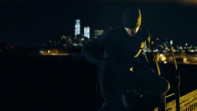 Charlie Cox in a black costume on a city roof in 'Daredevil.'