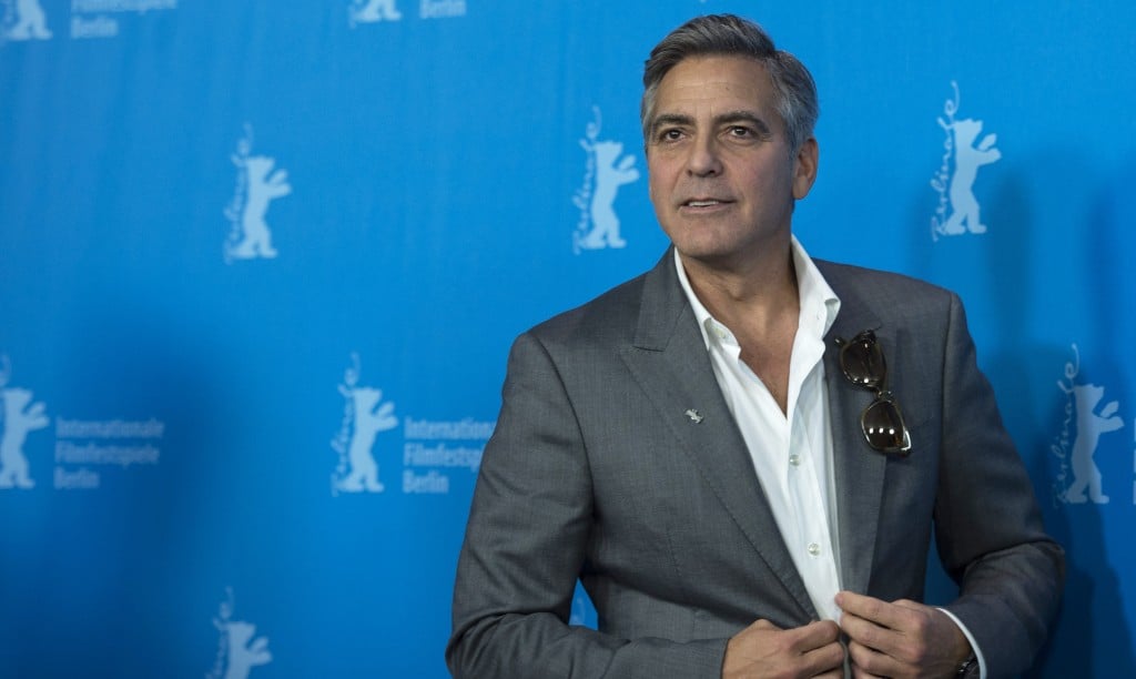 George Clooney adjusting his grey jacket on the red carpet.