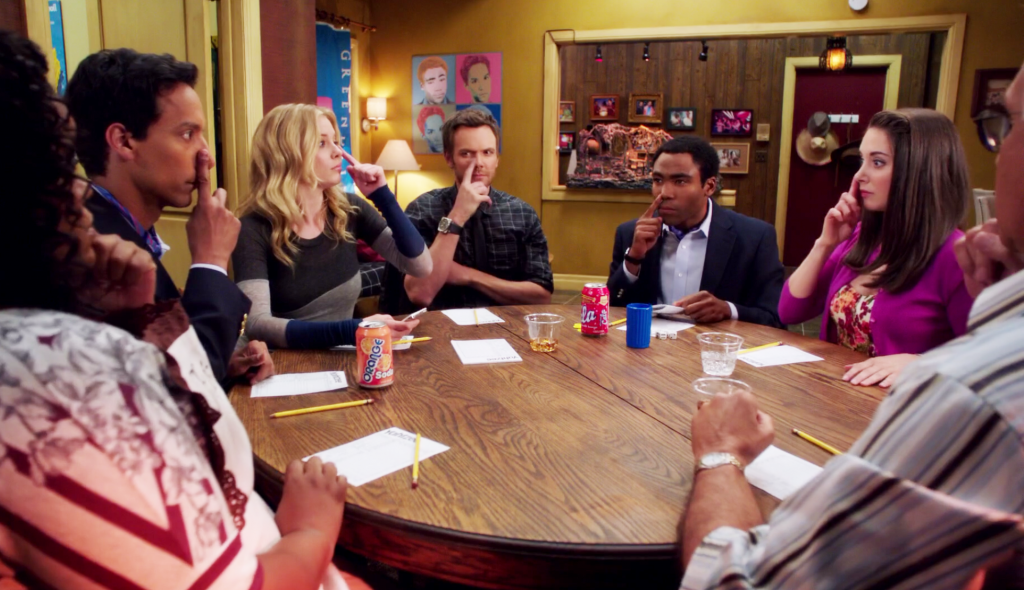 Yvette Nicole Brown as Shirley Bennett, Danny Pudi as Abed Nadir, Gillian Jacobs as Britta Perry, Joel McHale as Jeff Winger, Donald Glover as Troy Barnes, Alison Brie as Annie Edison, and Chevy Chase as Pierce Hawthorne sitting at a table with paper, pencils, and drinks with their fingers on their noses in a classroom on Community