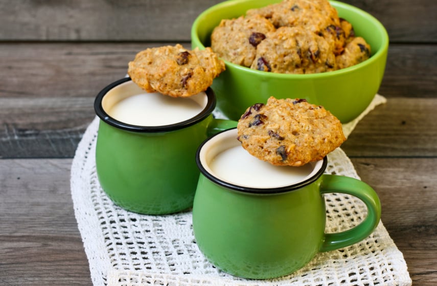 pile of oatmeal raisin cookies with two mugs of milk