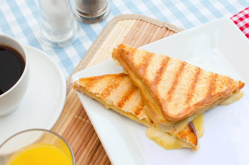 Grilled cheese sandwich on a platter along with coffee and orange juice