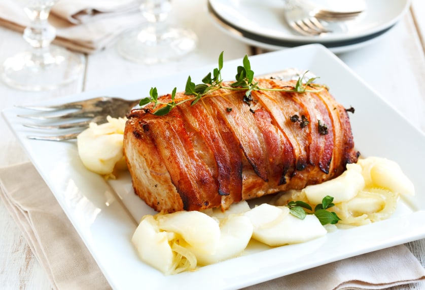 bacon wrapped pork on a serving platter surrounded by apples