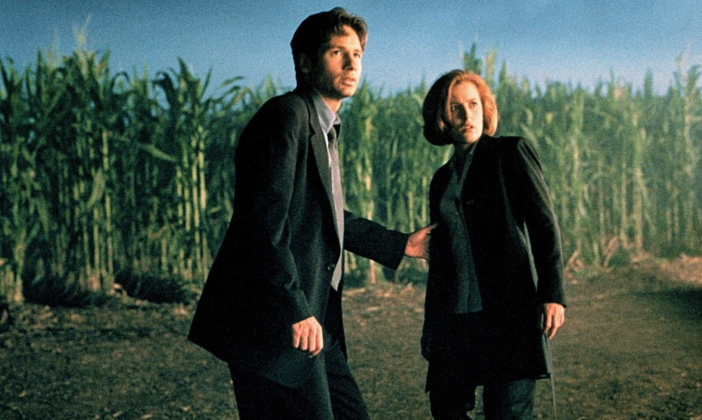 David Duchovny and Gillian Anderson stand next to each other in fear in front of a corn field
