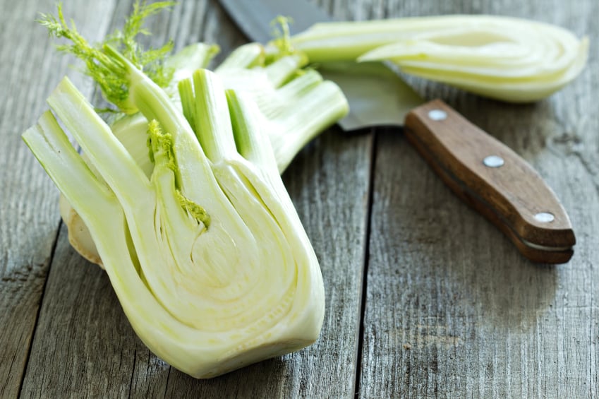 whole fennel bulb cut in half next to a knife on a wooden board