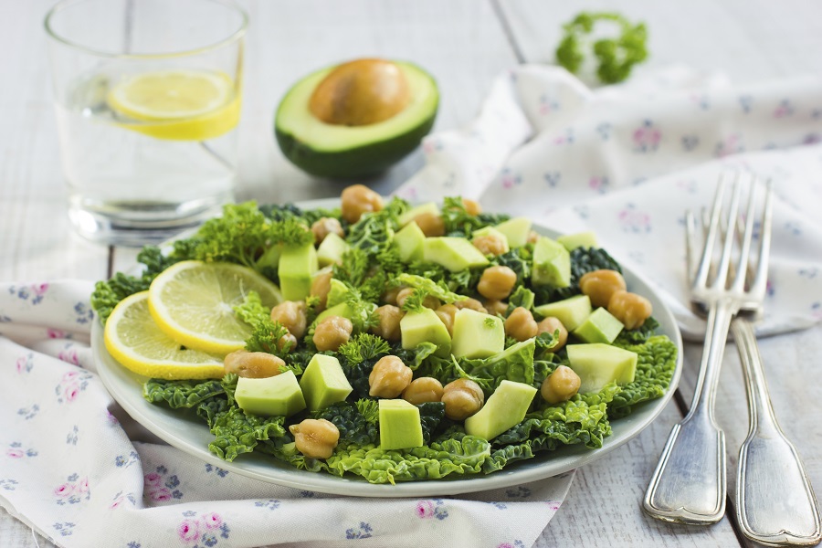 kale salad with chickpesas, avocado, and lemon wheels on a white plate