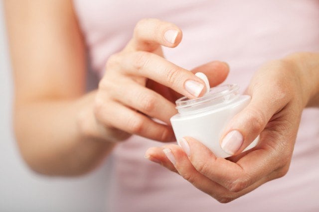 Woman dipping her fingers into a jar of cream