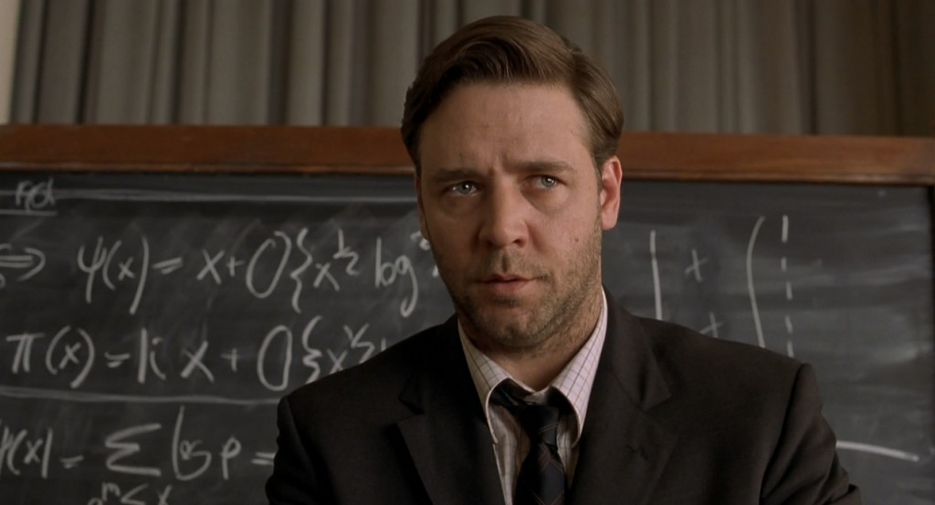 Russell Crowe is in a suit and is standing in front of a chalk board.