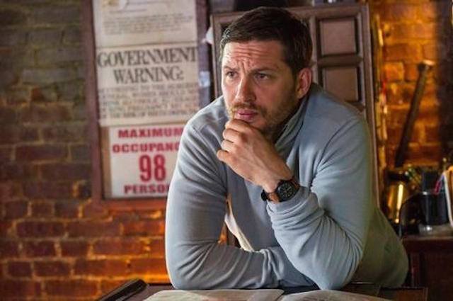 Tom Hardy rests his chin in his hands on a counter