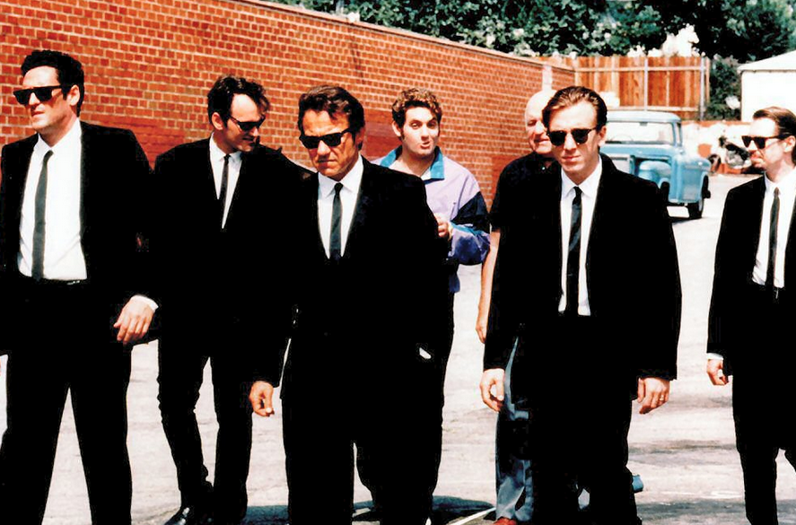 The cast of Reservoir Dogs are walking outside in black suits.