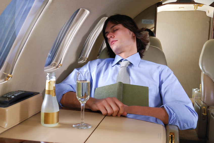 man sleeping on plane with a glass of Champagne in front of him