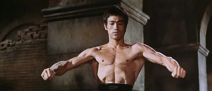 Bruce Lee has his arms out and is flexing.