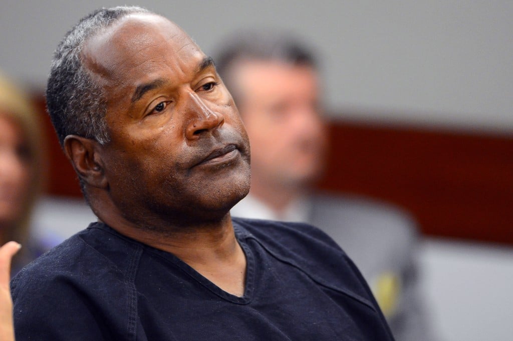 OJ Simpson wearing a blue prison suit, sitting in a courtroom with his head tilted back slightly