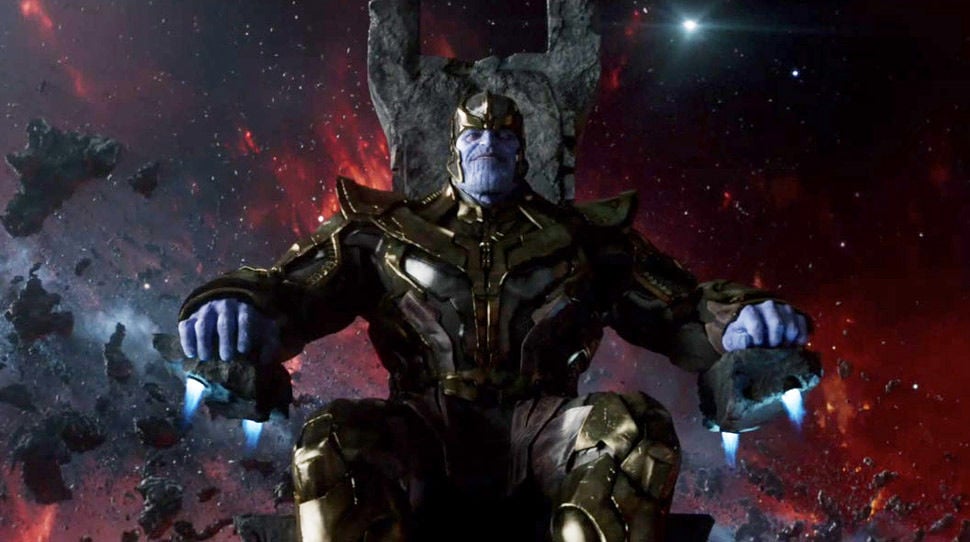 Thanos sits on his throne, looking directly at the camera with a slight smile