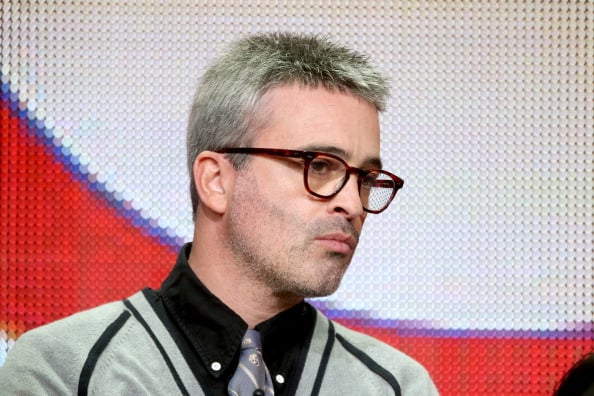 Alex Kurtzman wearing glasses and a tie, looking slightly down and to his left
