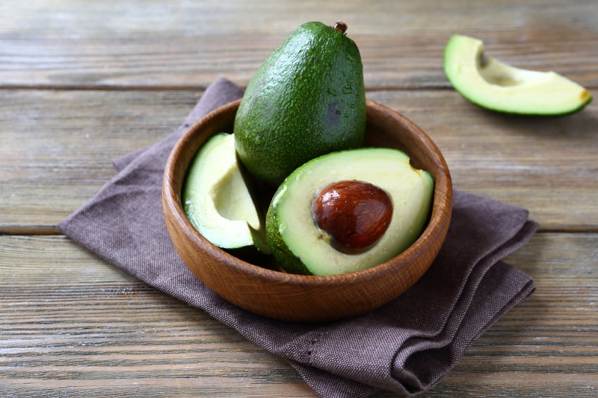 whole and halved avocado in a wooden bowl