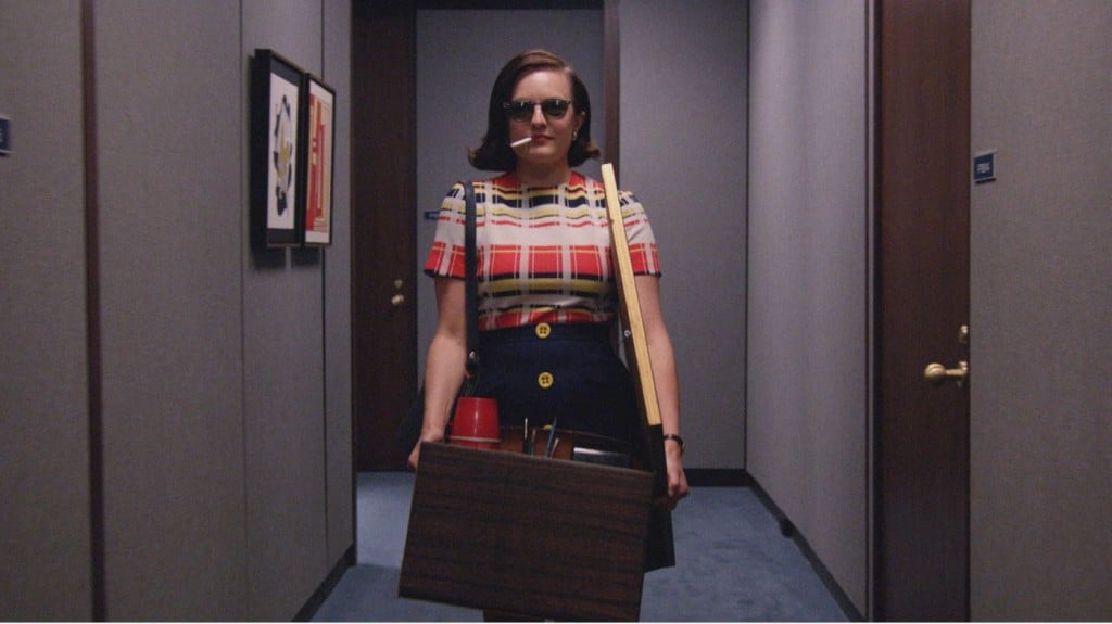 Peggy Olsen is walking down a hallway with a box of her things.