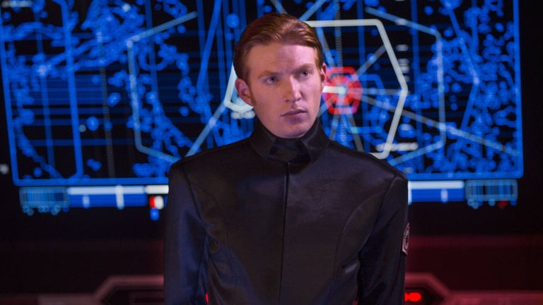 General Hux, looking off to the right, wearing a crisp officer's uniform in front of a blue digital readout