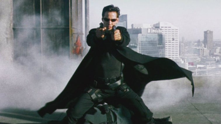 Keanu Reeves is on a rooftop and is holding up two guns in The Matrix.