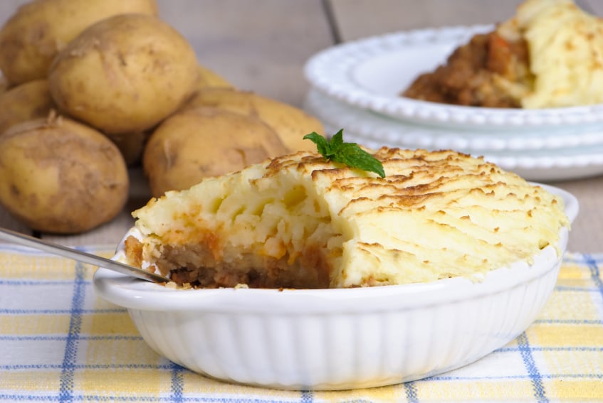 white casserole dish filled with shepherd's pie being scooped out