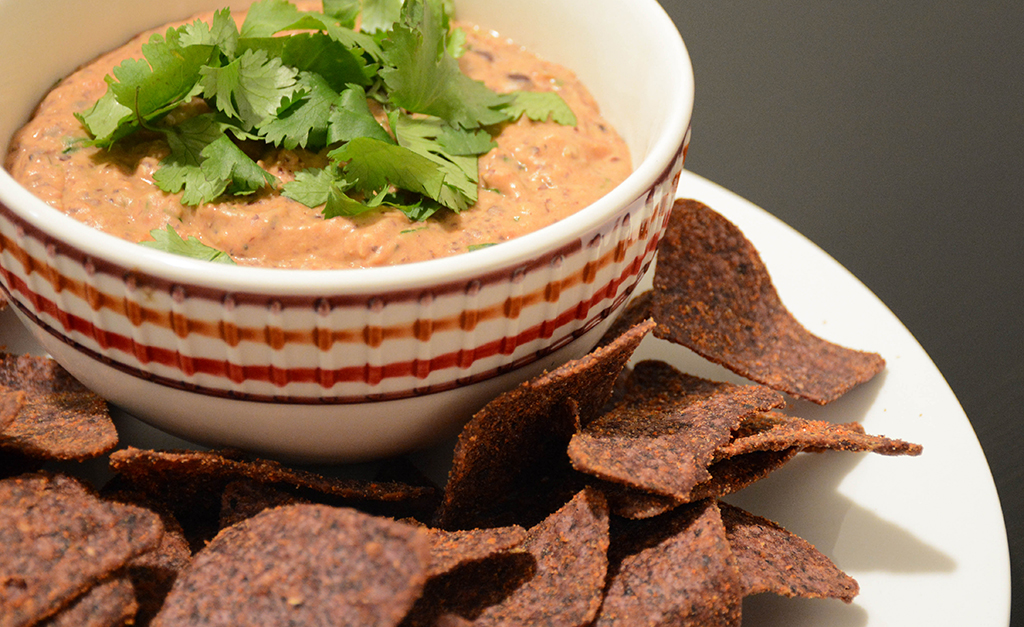 creamy black bean dip in a bowl with blue corn tortilla chips and cilantro