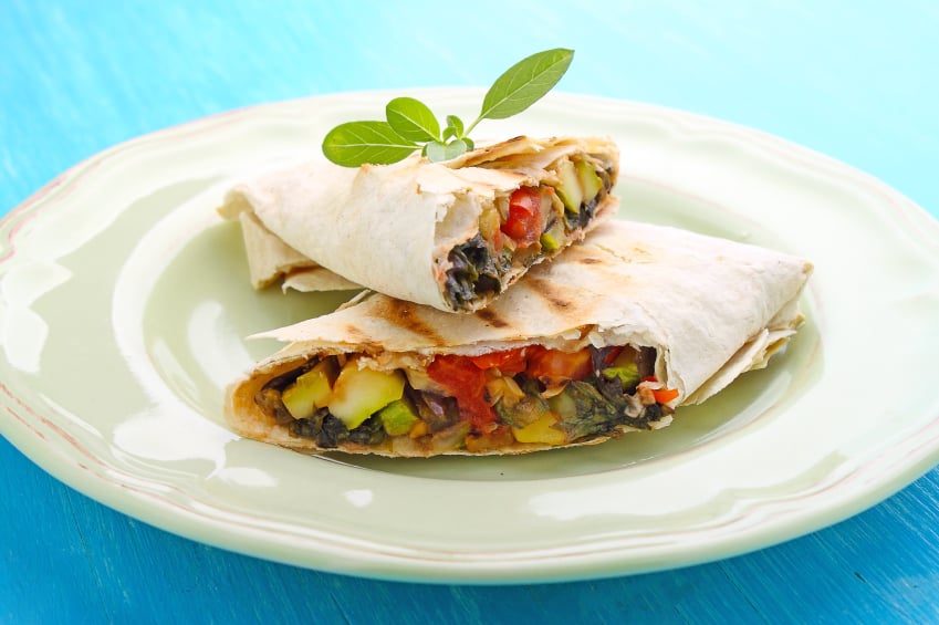 burrito with grilled vegetables and sauce on a white plate