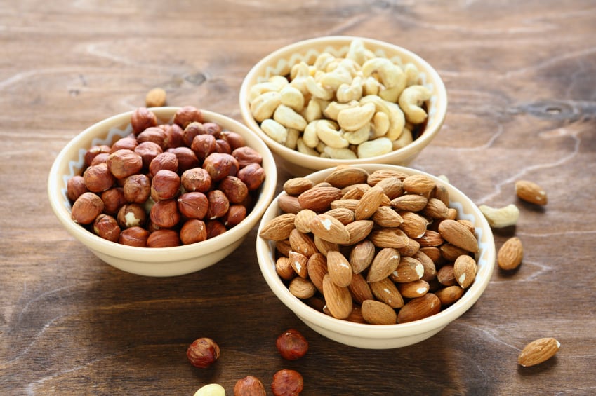 bowls of almonds, hazelnuts, and cashews sitting on a wooden counter