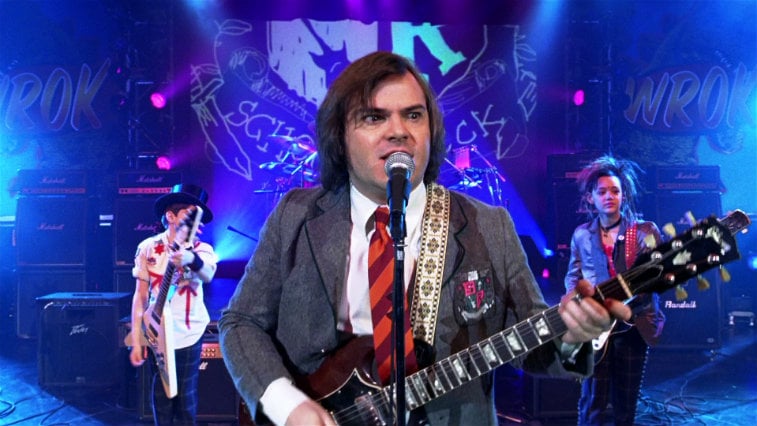 Jack Black wearing a suit, playing a guitar, and singing 