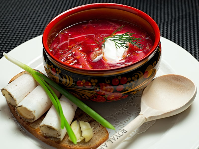 bowl of beet borscht with dill, sour cream and a side of buttered bread