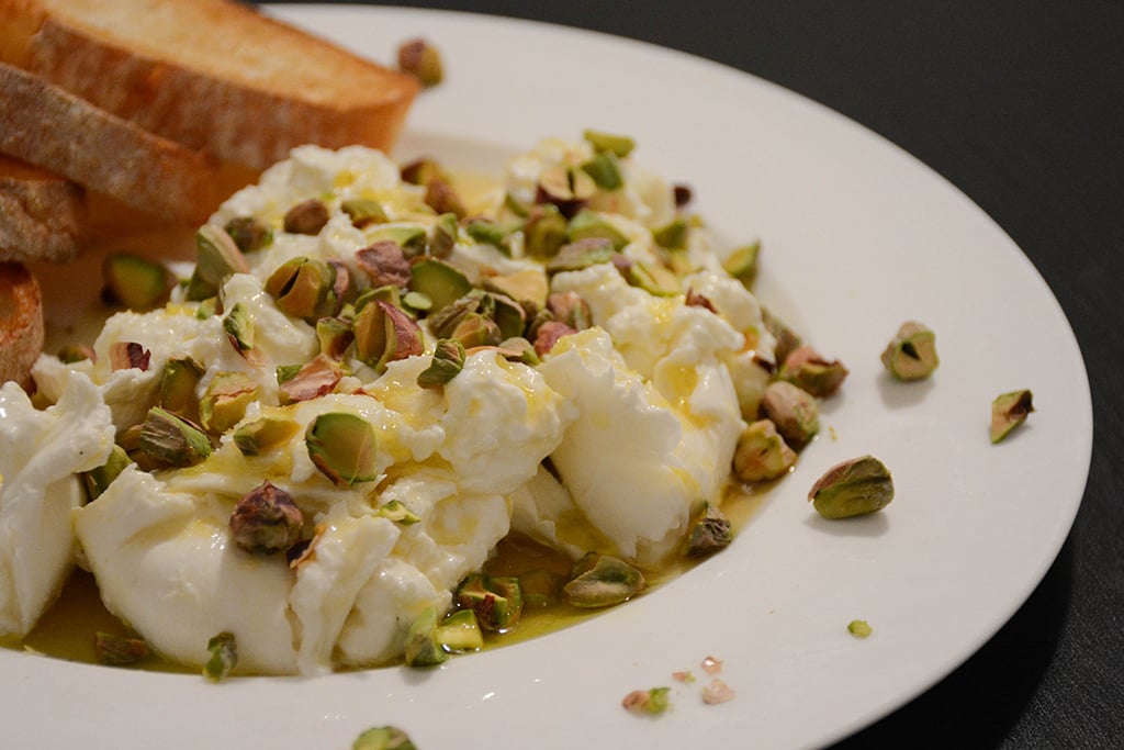 Burrata with honey-lemon dressing and pistachios on a white plate with toast
