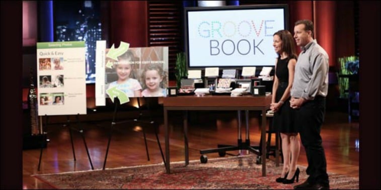 Julie and Brian Whiteman are in front of pictures and examples of Groovebook on Shark Tank.