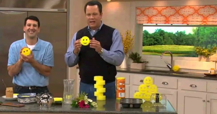 Two men are holding Scrub Daddy sponges in a fake kitchen.
