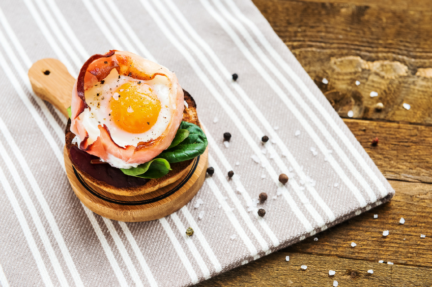 image of baked egg wrapped in bacon on top of spinach and toast