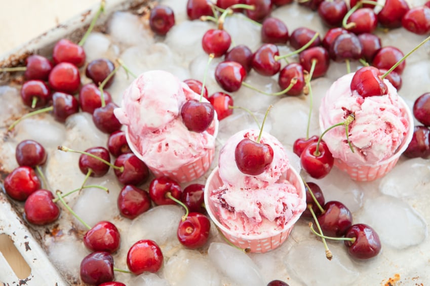 three cups filled with cherry ice cream surrounded by cherries