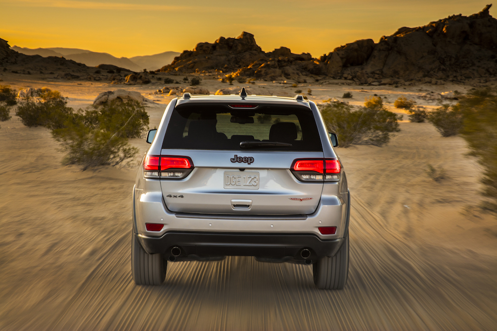 Rear view of a silver Jeep driving through the sand.