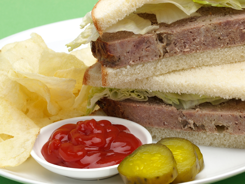 close up of a meatloaf sandwich with ketchup and pickles