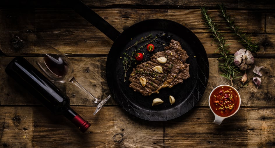 rib eye steak in a cast-iron skillet with a bottle of wine