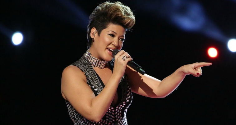 Tessanne Chin is singing and pointing to the left of the stage on The Voice.