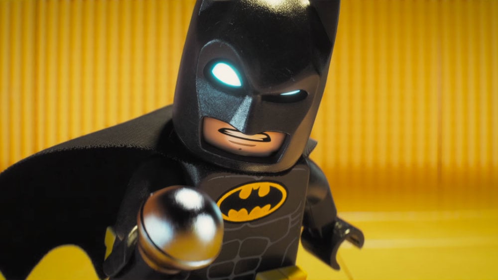 Lego Batman holds up a microphone and scowls at the camera