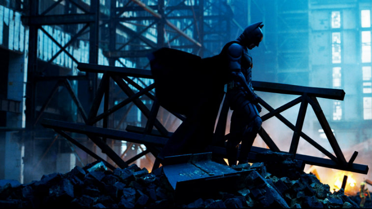 The silhouette of Christian Bale's Batman standing in wreckage in The Dark Knight