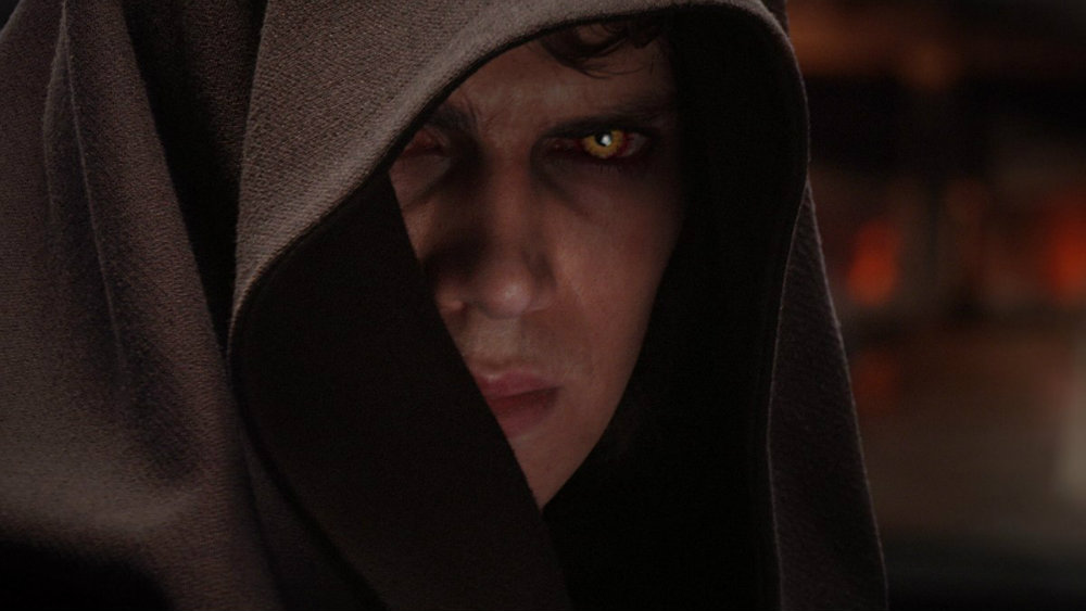 Anakin wearing a brown hood, with sinister yellow eyes, angrily staring into the camera