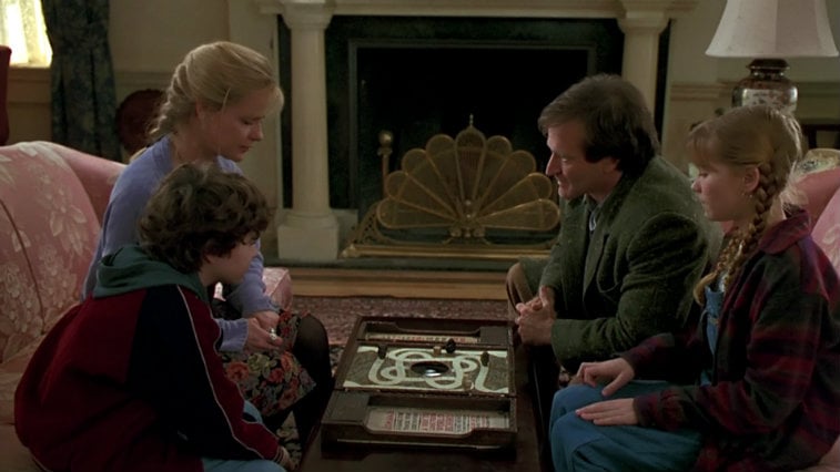 The cast of Jumanji gathers around the game board in a living room preparing to roll the dice