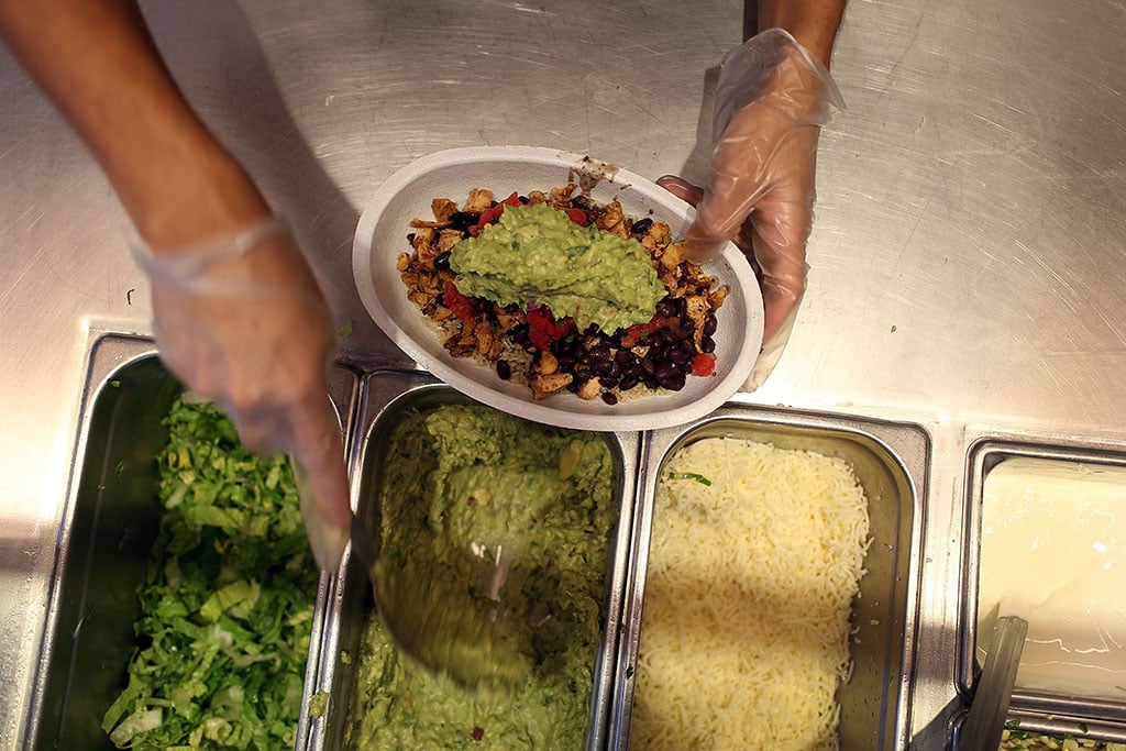 employee assembling a burrito bowl with guacamole at a chipotle
