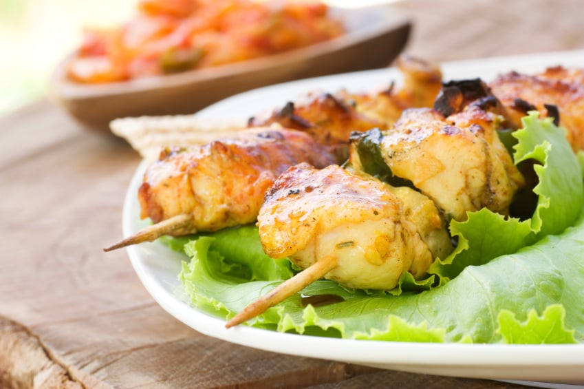close up of chicken skewers on a bed of lettuce with a tomato relish in the background