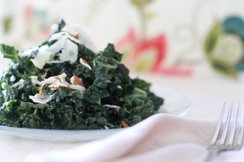 Tuscan kale salad on a white plate topped with chopped almonds and shaved Parmesan cheese