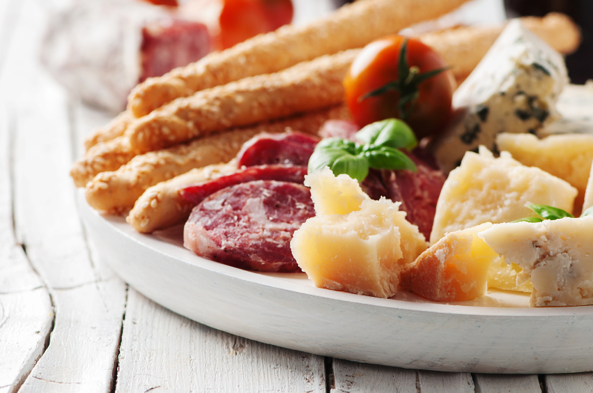 close-up of an Italian antipasto platter with cheese, salami, tomatoes, and bread sticks